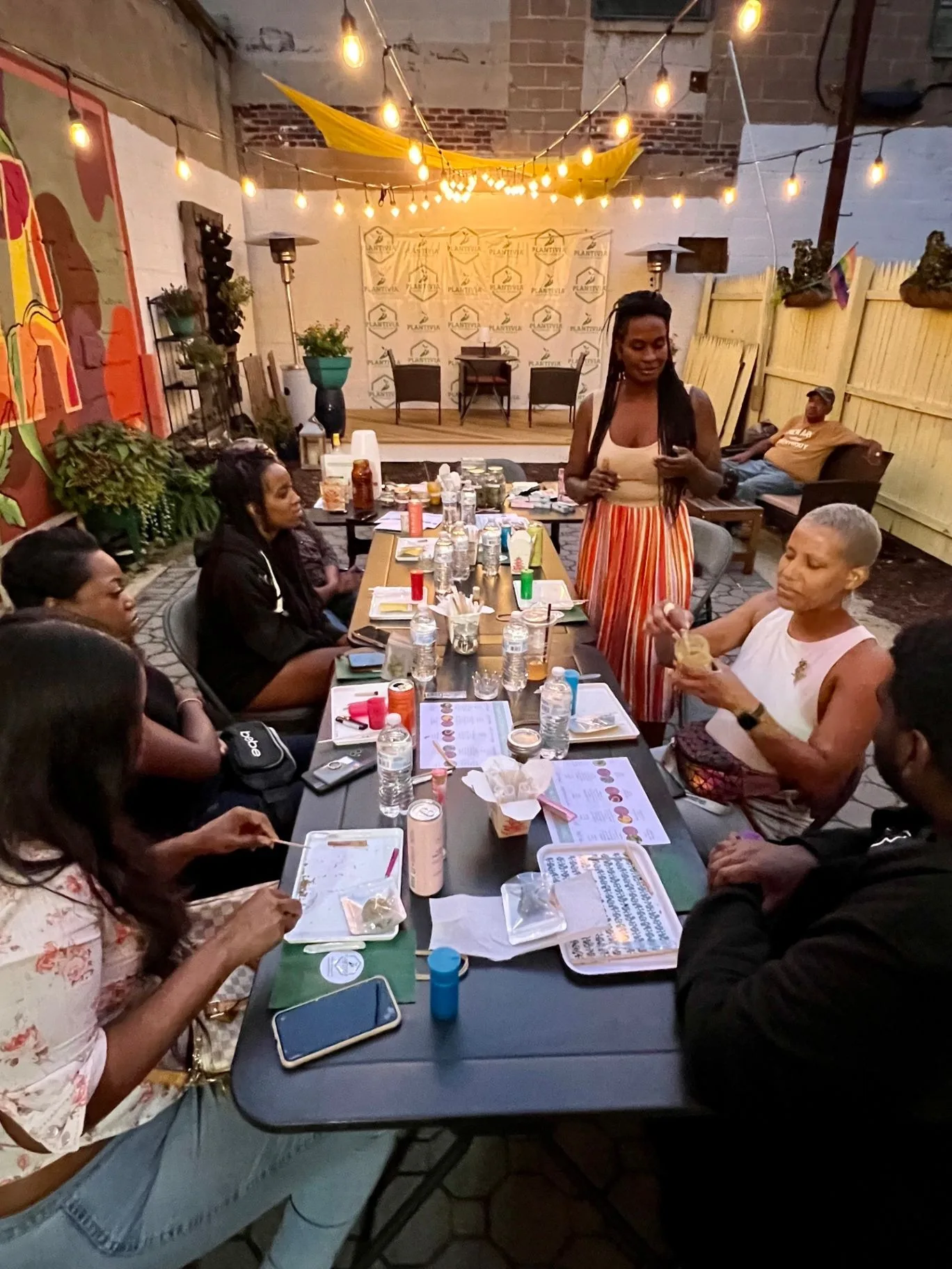 People gathered around a table at a Plantivia community event in a warmly lit outdoor space
